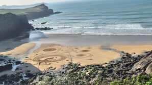 Un paisaje costero con una playa arenosa, acantilados rocosos y un mar tranquilo.
