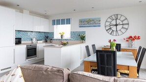 Una cocina moderna con armarios blancos, una isla central y una zona de comedor con mesa y sillas.
