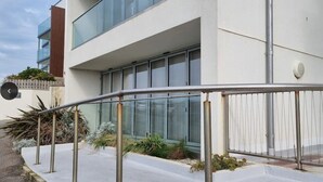 Un edificio moderno con fachada blanca, ventanas amplias y una cerca metálica al frente.