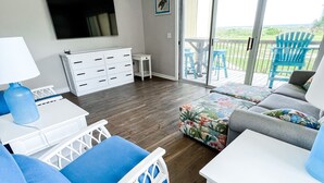 A modern living room with a sofa, a coffee table, and a TV mounted on the wall. - Oceanfront Condo w/Views, Pool + Parking (Surf City)