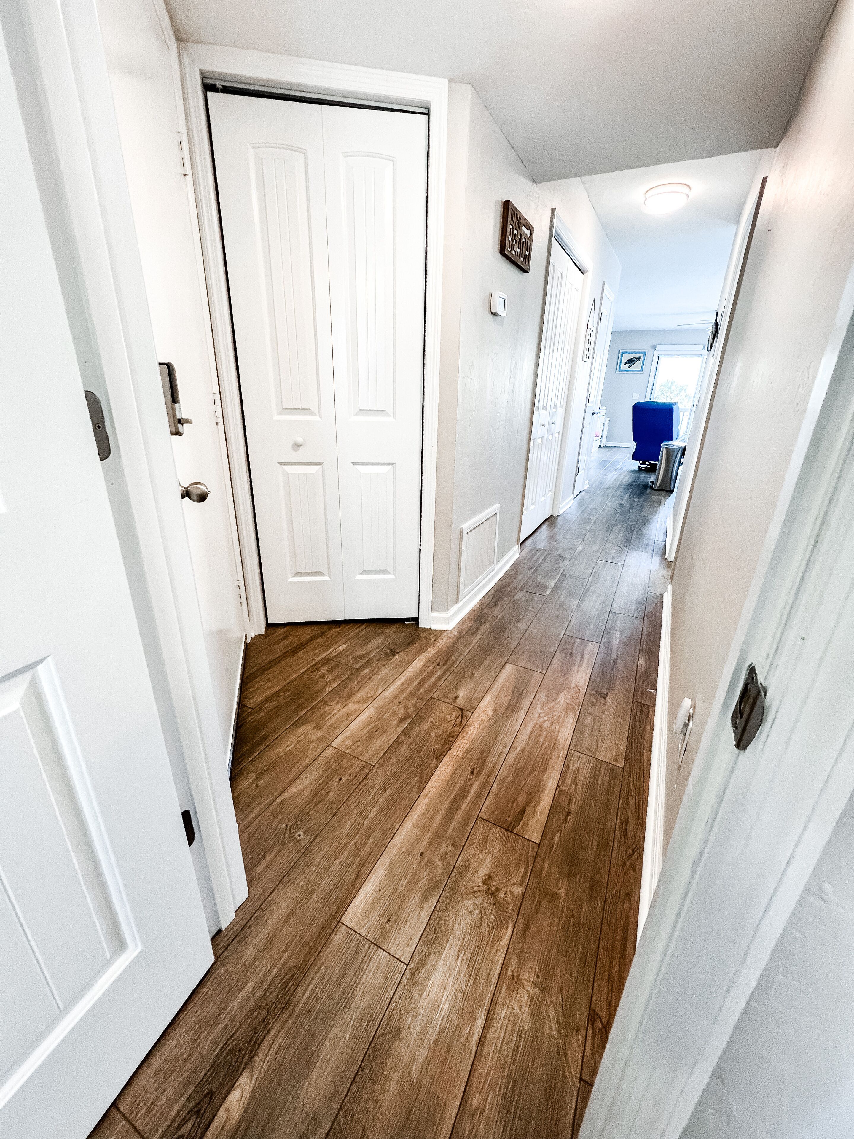 A hallway with wooden flooring, white doors, and a blue object in the distance.