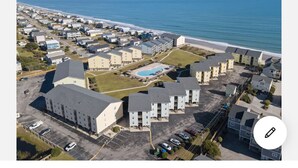An aerial view of a coastal residential area with multiple apartment buildings, a swimming pool, and a beach in the background. - Oceanfront Condo w/Views, Pool + Parking (Surf City)