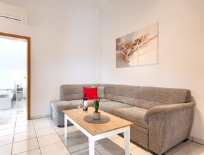 Uma sala de estar moderna com um sofá cinzento, uma mesa de centro de madeira e uma almofada vermelha.
