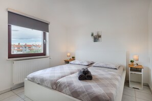 Quarto com cama, duas mesas de cabeceira, janela com vista e uma obra de arte na parede.