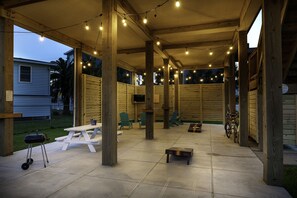 A covered outdoor patio with picnic tables, string lights, and a barbecue grill.