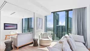 A modern living room with a sofa, a coffee table, and a chair. There is a large window with a view of buildings. - Signature 2B2B Stunning Chic Guest Fav +OceanView (Broadbeach)