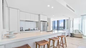 A modern kitchen with a large island, bar stools, and a view of the city. - Signature 2B2B Stunning Chic Guest Fav +OceanView (Broadbeach)