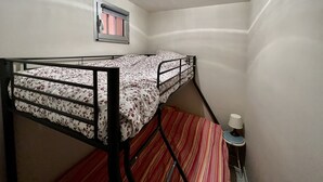 Un lit superposé avec une couvre-lit à motifs floraux, une fenêtre avec un rideau et une petite table avec une lampe.
