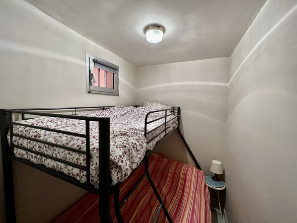A bunk bed with a floral bedspread, a window with a curtain, and a small table with a lamp. - Family apartment with Racou center label (argeles sur mer)