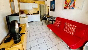 Un espace de vie compact comprenant un coin cuisine, un coin repas et un canapé rouge.