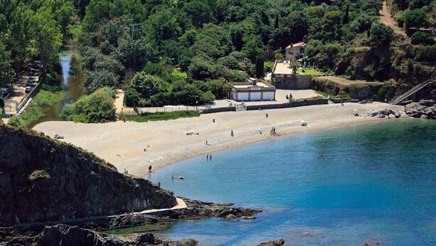 Une plage côtière avec des affleurements rocheux, une étendue de sable et un bâtiment doté d’un toit et de fenêtres.