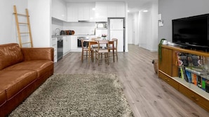 Ein modernes Wohnzimmer mit einer braunen Ledersofa, einem Essbereich mit Tisch und Stühlen, einer Küche mit weißen Schränken und einem Fernseher auf einem Holzboden.