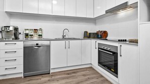 Eine moderne Küche mit weißen Schränken, einem Geschirrspüler, einem Backofen und einer Kaffeemaschine.