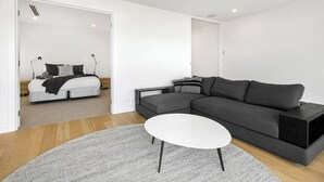 A modern living room with a sectional sofa, a white coffee table, and a bed in the adjacent room. - Strangeways Stays! -Slps 10, 4 Bdrm, Oceanview (Port Elliot)