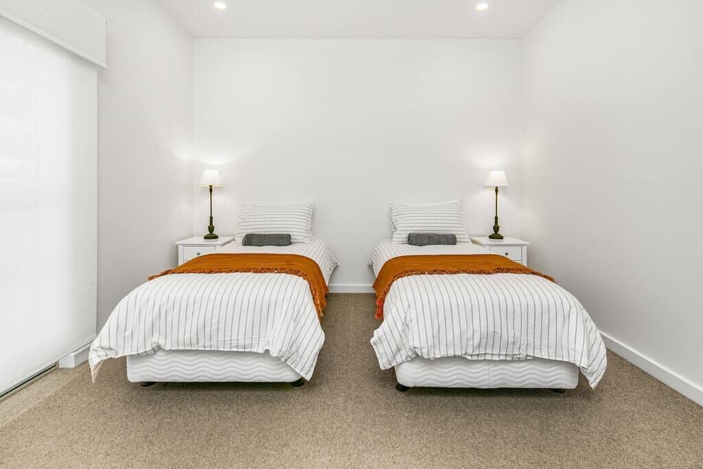 Ein Zweibettzimmer mit zwei Betten, jeweils mit weiß gestreifter Bettdecke und orangefarbener Tagesdecke.