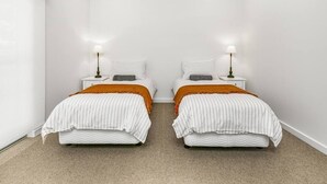 A twin bedroom with two beds, each with a white striped bedspread and an orange throw blanket. - Strangeways Stays! -Slps 10, 4 Bdrm, Oceanview (Port Elliot)