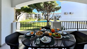 A balcony with a table set for breakfast, overlooking a pool and a building. - VILAMOURA GARDEN VIEW 1 WITH POOL by HOMING (Vilamoura)