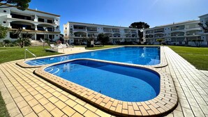 A swimming pool with a tiled deck, surrounded by a building with multiple balconies and a clear sky. - VILAMOURA GARDEN VIEW 1 WITH POOL by HOMING (Vilamoura)