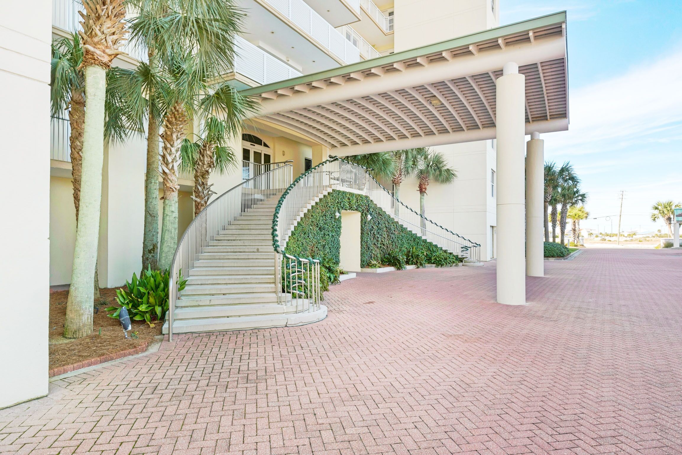 A hotel entrance with a curved staircase, palm trees, and a covered walkway.