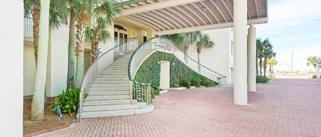 A hotel entrance with a curved staircase, palm trees, and a covered walkway.