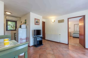 Een gezellige, kleine ruimte met een kitchenette, een televisie op een standaard en een zithoek met een bankje en twee gele mokken.