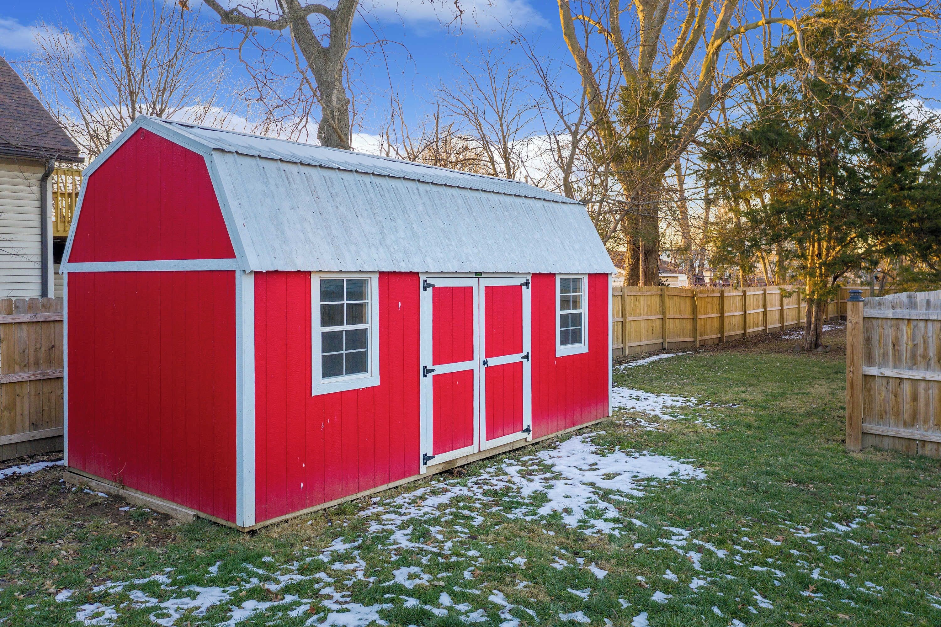 A red wooden shed with a sloped roof, white trim, and two windows.