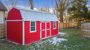 A red wooden shed with a sloped roof, white trim, and two windows.