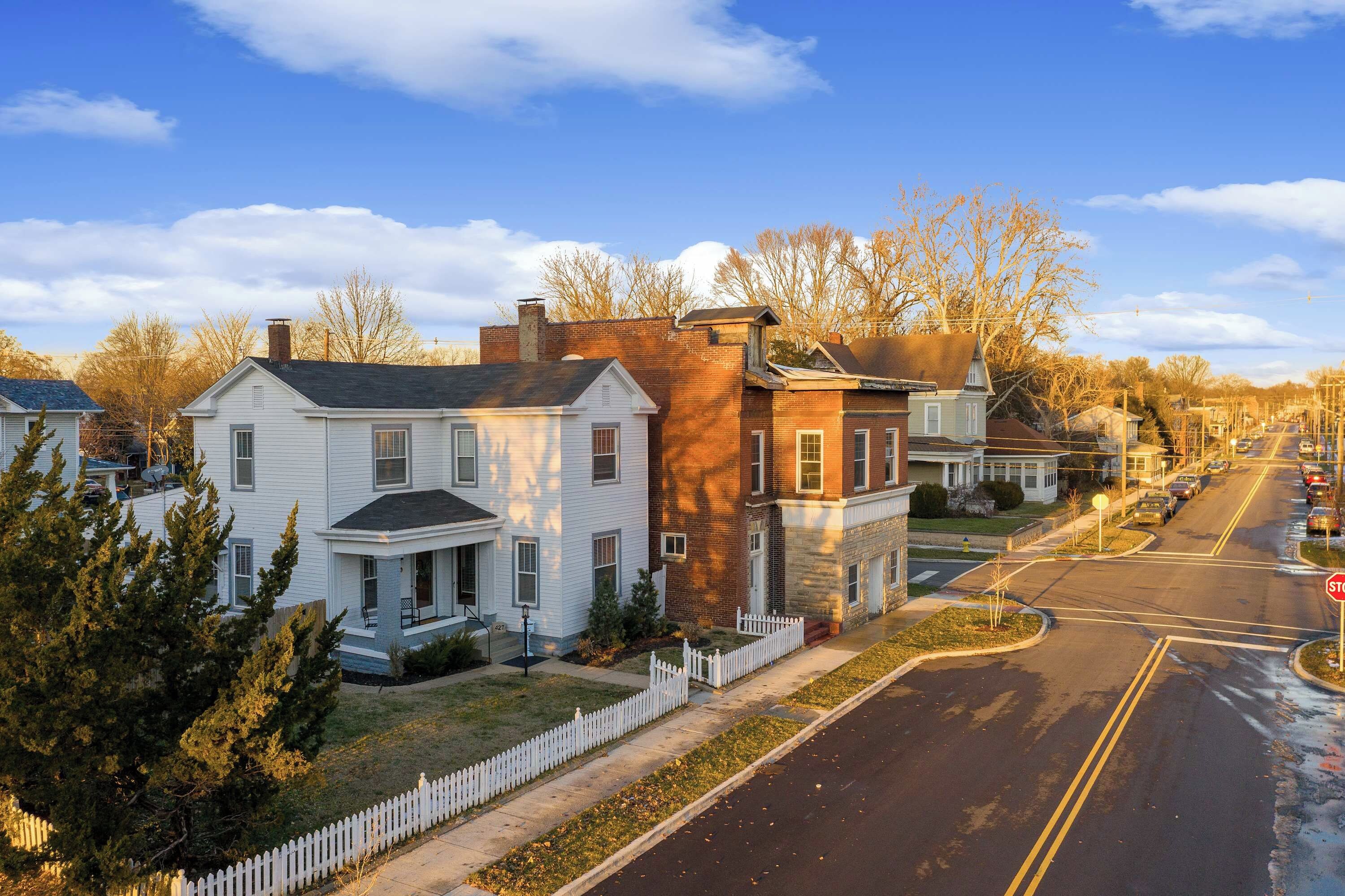 A residential street with houses, a white picket fence, and a stop sign.
