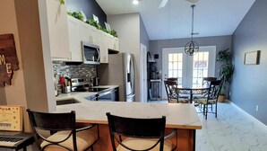 Une cuisine moderne avec des meubles blancs, un plan de travail en marbre et un coin repas comprenant une table et des chaises.