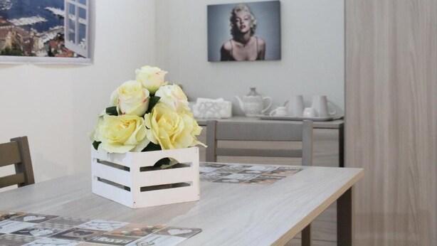 Una mesa de comedor con un arreglo floral blanco, un cuadro en la pared y vista a un paisaje montañoso a través de una ventana.