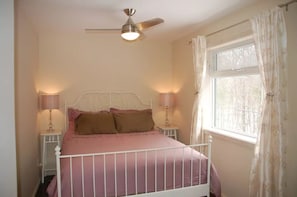 Une chambre à coucher avec un lit, deux lampes de chevet, un ventilateur de plafond et une fenêtre avec des rideaux.