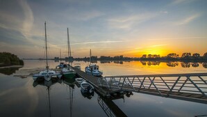 Un port de plaisance paisible, où plusieurs bateaux sont amarrés à un quai en bois, au moment du coucher du soleil.