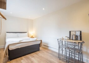 Habitación de hotel con cama, mesita de noche con lámpara, una pequeña mesa redonda con silla y cafetera.