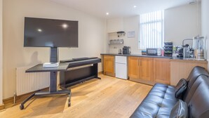 Una cocina moderna con una televisión de pantalla plana, un escritorio negro, un refrigerador blanco, armarios de madera y un sofá de cuero negro.