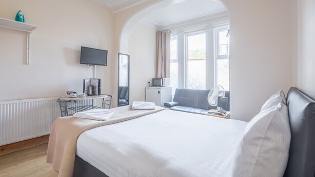 Habitación de hotel con una cama grande, un escritorio con computadora, televisor y ventana con cortinas.