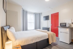 A hotel room with a bed, a desk with a microwave, a refrigerator, a TV, and a window with curtains.