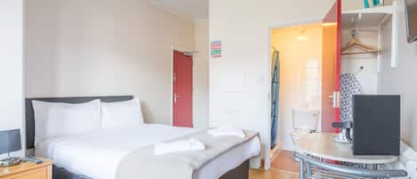 Una habitación de hotel con cama, mesita de noche, silla y escritorio con computadora.