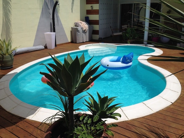 Enjoy a refreshing swim in the pool surrounded by lush greenery and a wooden deck.