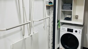 A laundry room with a front-loading washing machine, a drying rack, and a shelving unit with folded clothes. - The Birds Nest in Central Phoenix (Phoenix)