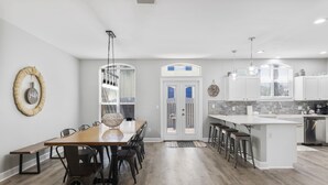 A modern kitchen with white cabinets, a wooden dining table, and bar stools. - Latitude Adjustment | Luxury Beach Retreat ☀️ | 15% Off July Weeks (Miramar Beach)