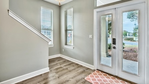 A hallway with a wooden floor, a chandelier, and a set of double doors leading outside. - Latitude Adjustment | Luxury Beach Retreat ☀️ | 15% Off July Weeks (Miramar Beach)