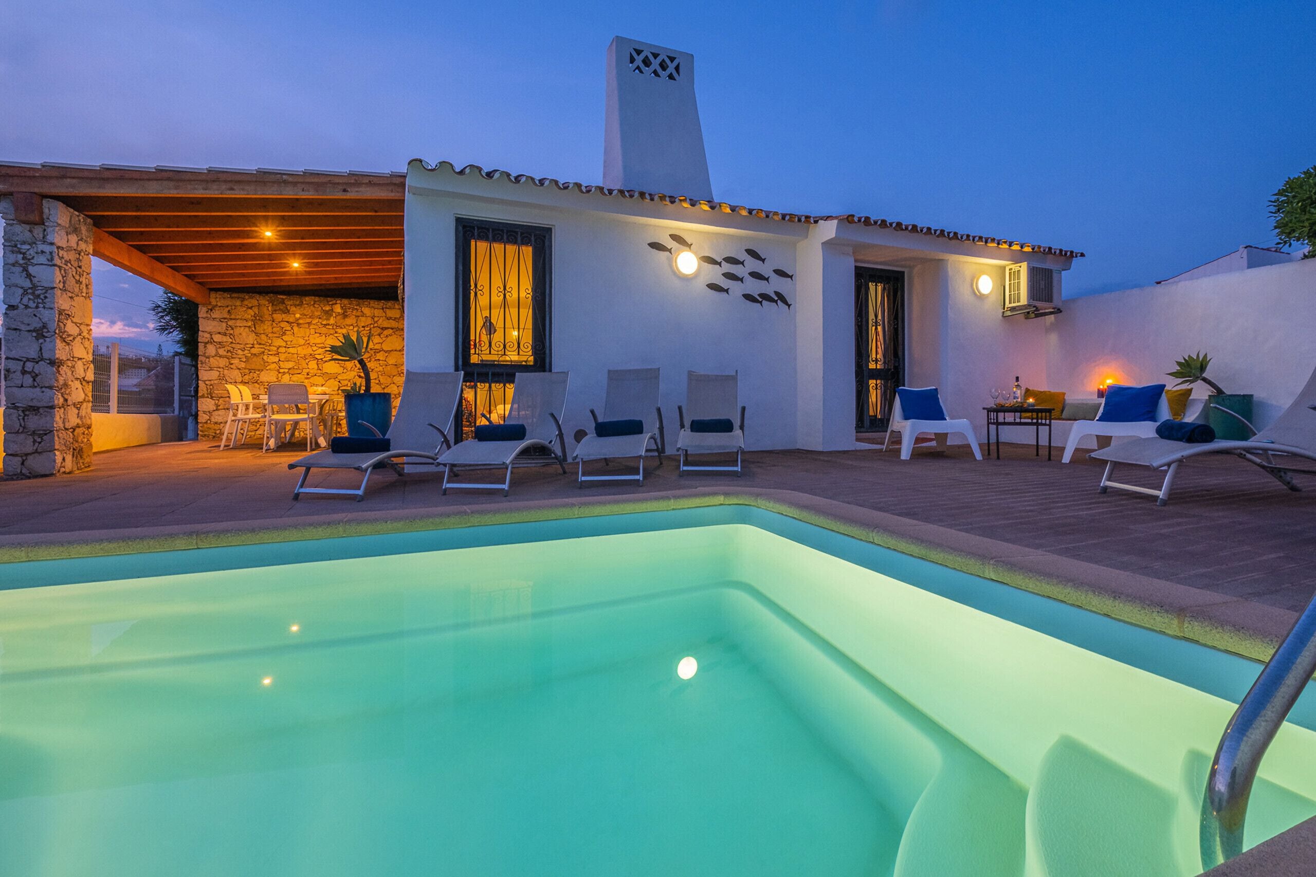 A poolside area with lounge chairs, a stone wall, and a covered seating area.