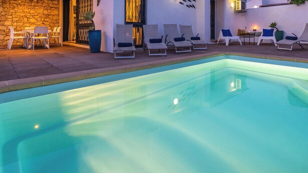 Una piscina con sillas de descanso y una mesa, rodeada de un muro de piedra y un edificio con balcón.