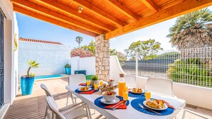Un espacio exterior para comer con una mesa lista para el desayuno, un pilar de piedra y vistas a una piscina.