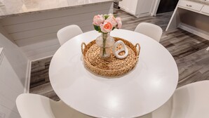 A round white table with a woven placemat, a vase with flowers, and a white decorative item. - Private Pool–Renovated Home for Groups/Getaways (Memphis)