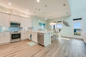 A spacious kitchen with white cabinetry, a central island, stainless steel appliances, and a view to the outdoors. - Whooping Crane Lane by Silver Sands Vacation Rentals (Port Aransas)