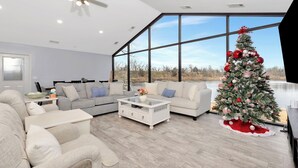 Un salon moderne avec une grande fenêtre, un ventilateur de plafond blanc et un sapin de Noël.
