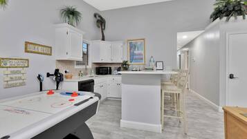 A modern kitchen with white cabinets, a central island, and a foosball table.