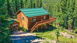 A wooden cabin with a green roof, a deck, and a staircase leading to the entrance.