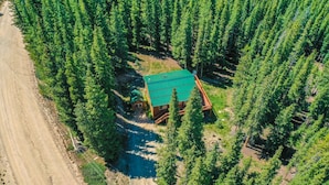 Ilmakuva mökistä, jonka ympärillä on tiheä metsä, ja mökkiin johtaa soratie.